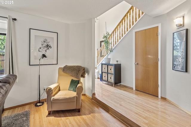 living area with baseboards, wood finished floors, and stairway