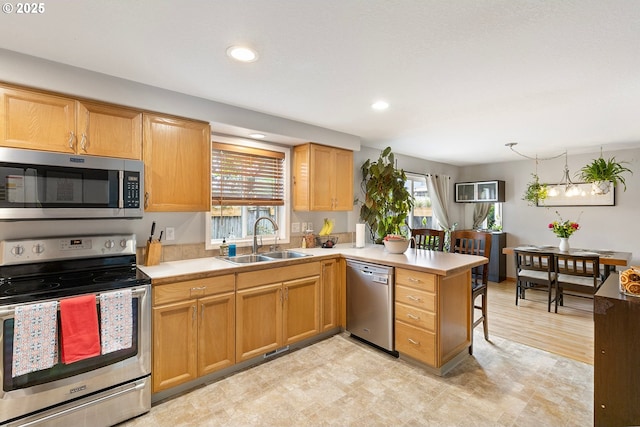kitchen with a peninsula, recessed lighting, light countertops, a sink, and appliances with stainless steel finishes