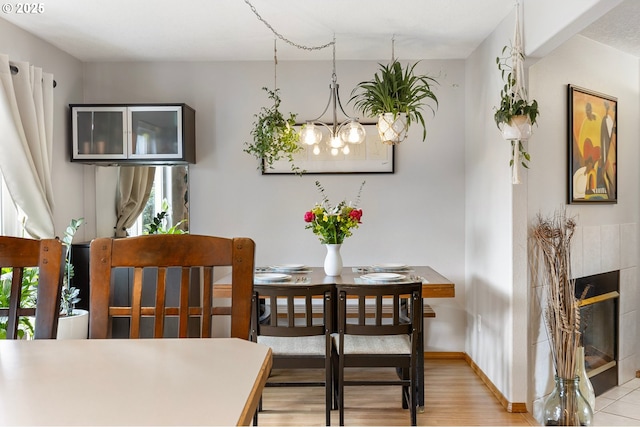 dining room with an inviting chandelier, baseboards, light wood-style flooring, and a tile fireplace