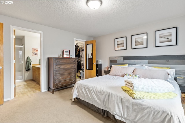 bedroom featuring a closet, light carpet, ensuite bathroom, a walk in closet, and a textured ceiling