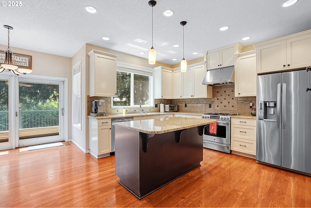 4710 SW Joshua St, Tualatin, OR 97062 - kitchen with appliances with stainless steel finishes, under cabinet range hood, light stone counters, backsplash, and light wood finished floors