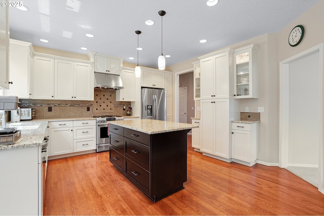 4710 SW Joshua St, Tualatin, OR 97062 - kitchen with stainless steel appliances, under cabinet range hood, white cabinets, dark brown cabinets, and decorative backsplash