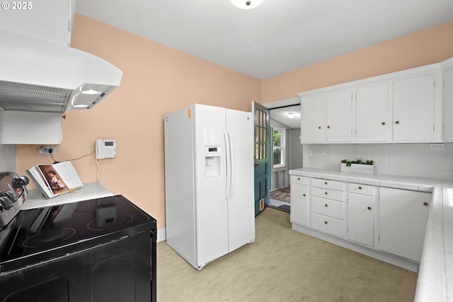 kitchen featuring white refrigerator with ice dispenser, black range with electric stovetop, tile counters, ventilation hood, and white cabinets