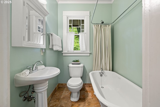 bathroom with stone tile floors, a freestanding bath, baseboards, toilet, and ornamental molding