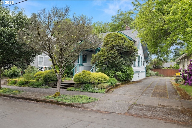 view of property hidden behind natural elements with driveway, a chimney, and fence