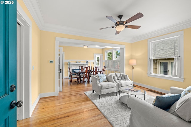 living room with ornamental molding, light wood-style flooring, baseboards, and ceiling fan