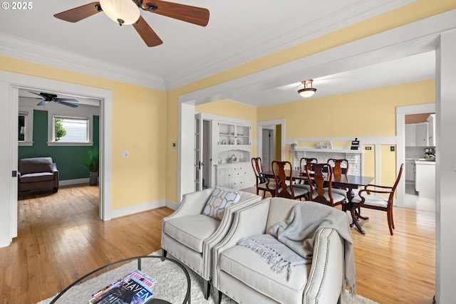 living area with a ceiling fan, light wood-style floors, baseboards, and ornamental molding