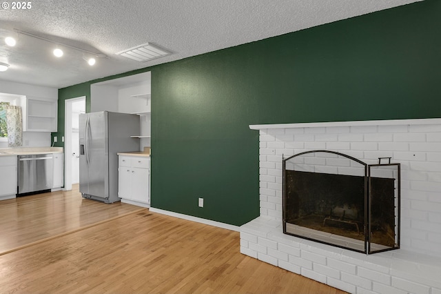 1437 Sequoia Ave, Springfield, OR 97477 - unfurnished living room with light wood finished floors, a textured ceiling, a brick fireplace, and baseboards