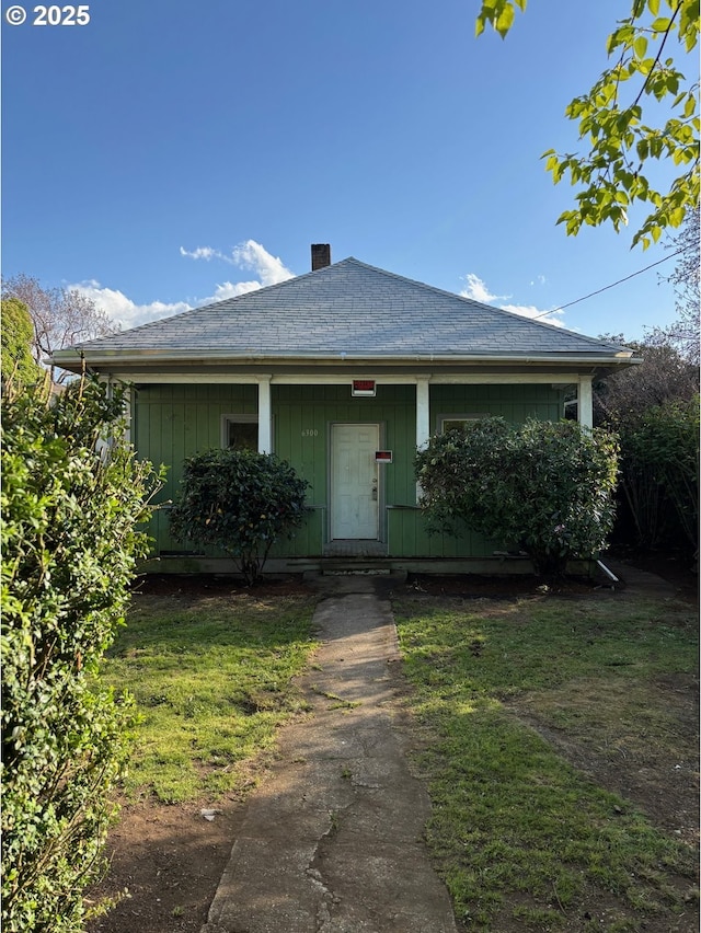 view of front facade featuring board and batten siding, a porch, a chimney, and a front yard