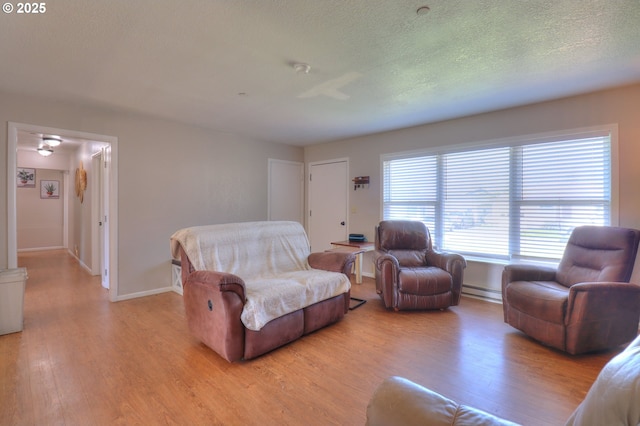 94178 9th St, Gold Beach, OR 97444 - living area featuring light wood-style flooring, a baseboard radiator, baseboards, a ceiling fan, and a textured ceiling