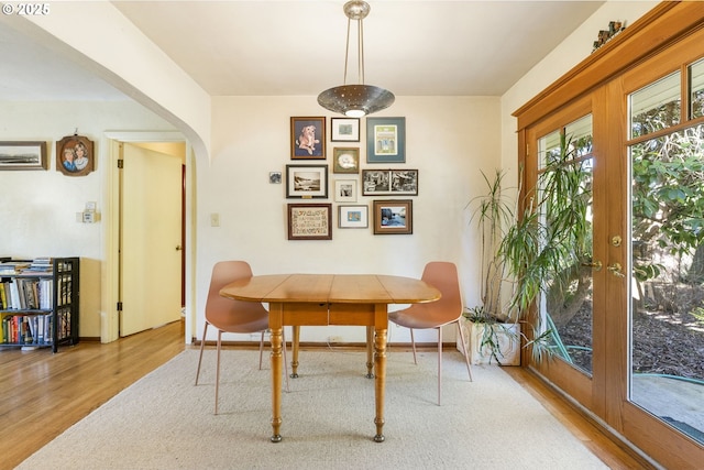 dining area featuring french doors, arched walkways, baseboards, and wood finished floors