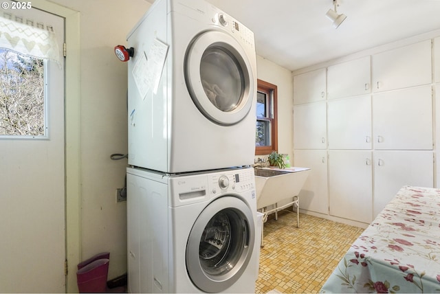 washroom with cabinet space, plenty of natural light, stacked washer and clothes dryer, and track lighting