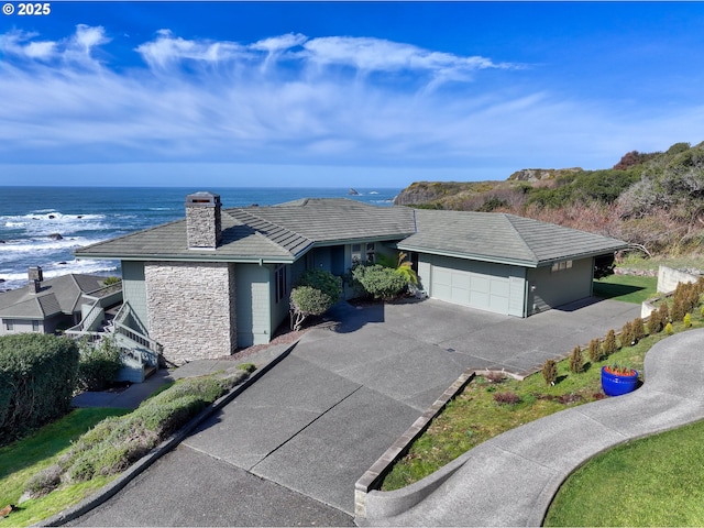 ranch-style home featuring a chimney, concrete driveway, a water view, an attached garage, and stone siding