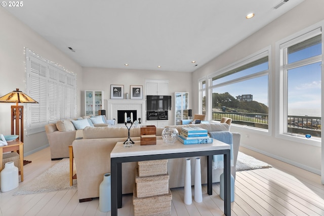 living room featuring recessed lighting, a fireplace, visible vents, baseboards, and light wood finished floors