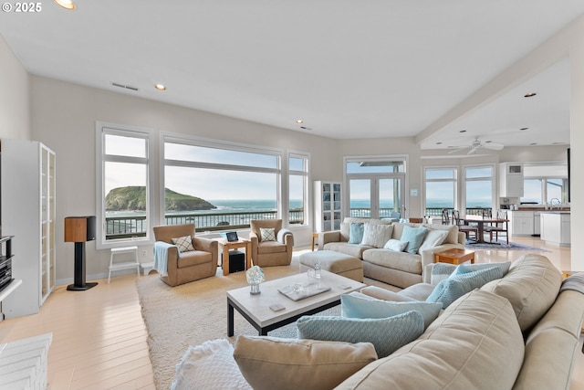 living area featuring recessed lighting, a water view, visible vents, baseboards, and light wood-style floors