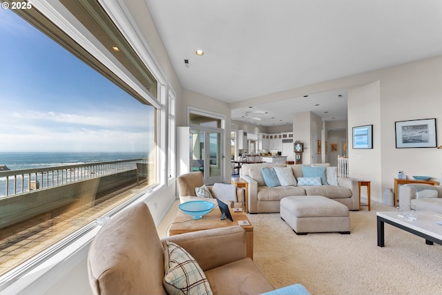 living area with a water view, plenty of natural light, light carpet, and baseboards