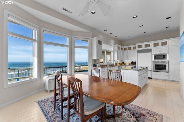 dining area with recessed lighting, a water view, visible vents, light wood-type flooring, and baseboards