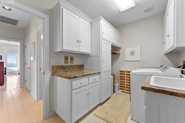 washroom featuring cabinet space, visible vents, light wood finished floors, and washer and dryer