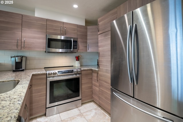 kitchen with decorative backsplash, appliances with stainless steel finishes, light tile patterned floors, light stone counters, and recessed lighting
