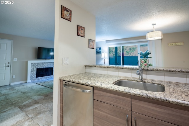 kitchen with light stone countertops, a sink, a fireplace, baseboards, and stainless steel dishwasher