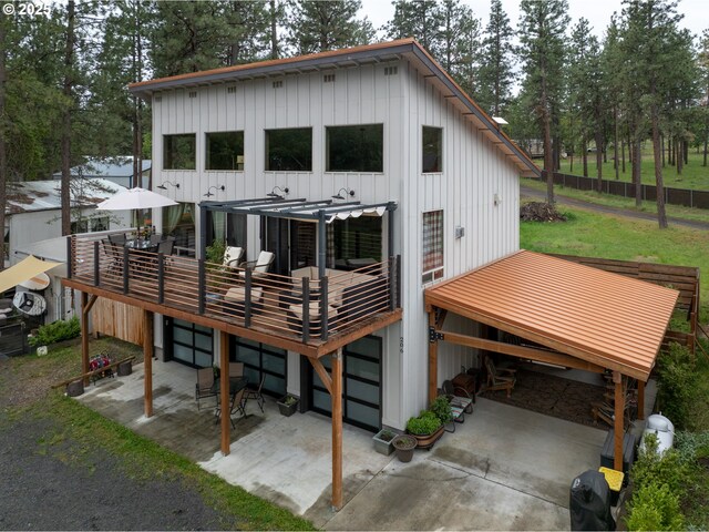 rear view of house featuring board and batten siding, a deck, a patio, and a lawn