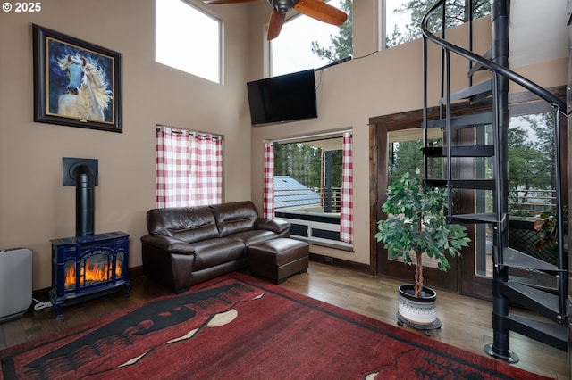 living room with a wood stove, hardwood / wood-style flooring, ceiling fan, healthy amount of natural light, and a towering ceiling