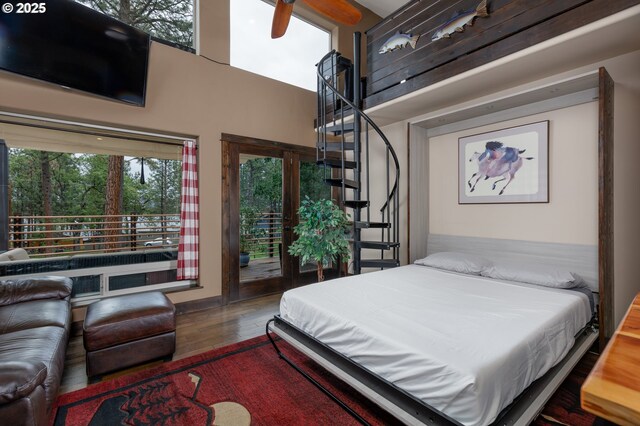 bedroom with access to exterior, wood finished floors, and a high ceiling