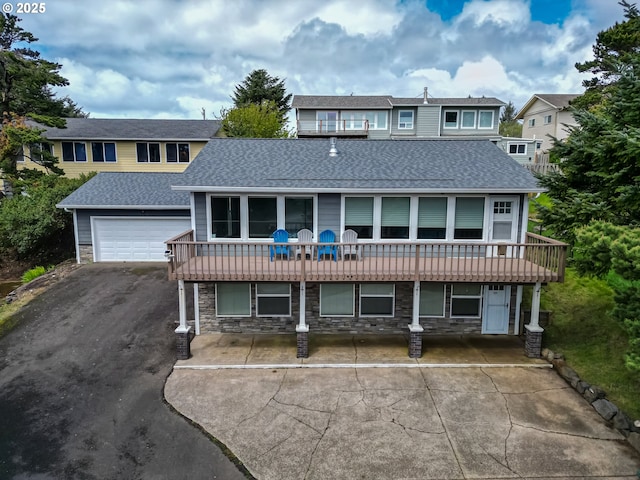 view of front of property with a deck, driveway, a shingled roof, and stone siding