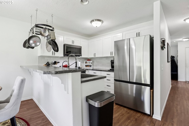 kitchen featuring a peninsula, appliances with stainless steel finishes, backsplash, and white cabinets