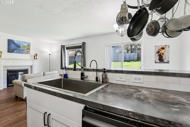 kitchen featuring dark countertops, dark wood-style flooring, a sink, and a tile fireplace