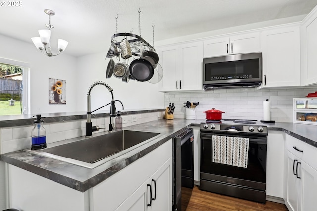 kitchen with dark countertops, backsplash, appliances with stainless steel finishes, white cabinetry, and a sink