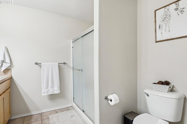 bathroom featuring toilet, vanity, a shower stall, baseboards, and tile patterned floors