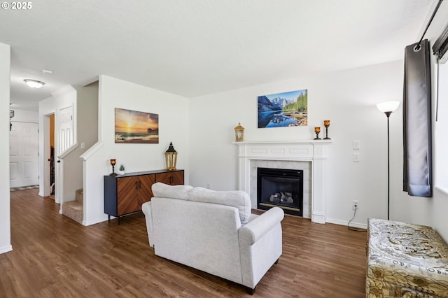 living room with dark wood-style floors, a tile fireplace, baseboards, and stairs