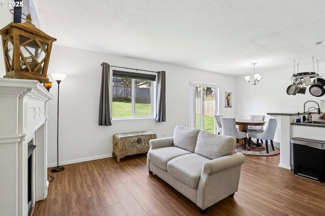 living area featuring baseboards, dark wood-style floors, an inviting chandelier, a textured ceiling, and a fireplace