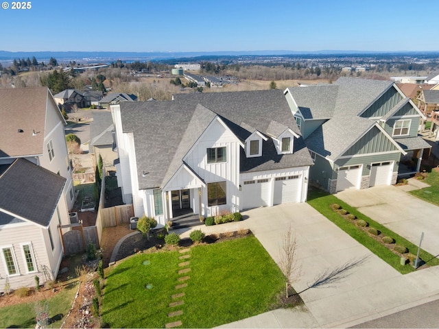 view of front facade featuring roof with shingles, concrete driveway, board and batten siding, a front yard, and a residential view