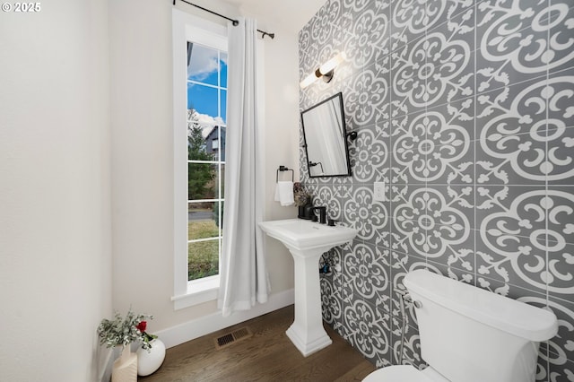 half bath featuring toilet, baseboards, visible vents, and wood finished floors