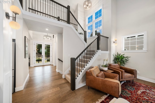 foyer entrance featuring baseboards, stairway, wood finished floors, french doors, and a chandelier