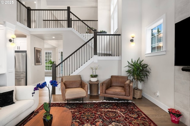 living area featuring stairway, a towering ceiling, baseboards, and wood finished floors