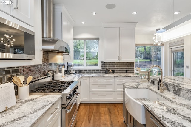 kitchen featuring a sink, appliances with stainless steel finishes, wall chimney exhaust hood, and white cabinetry