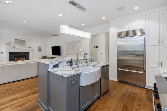 kitchen featuring light wood-style flooring, gray cabinets, stainless steel appliances, white cabinetry, and a sink