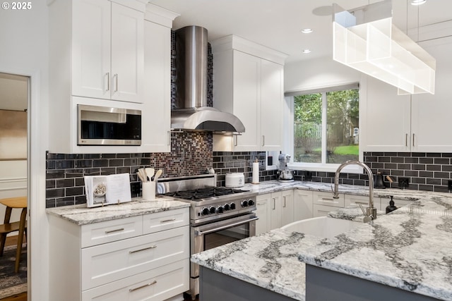 kitchen with a sink, decorative backsplash, white cabinets, appliances with stainless steel finishes, and wall chimney exhaust hood