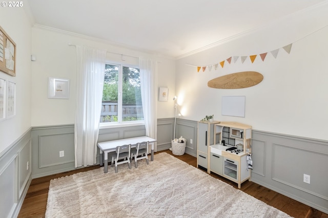 recreation room featuring wainscoting, crown molding, and wood finished floors