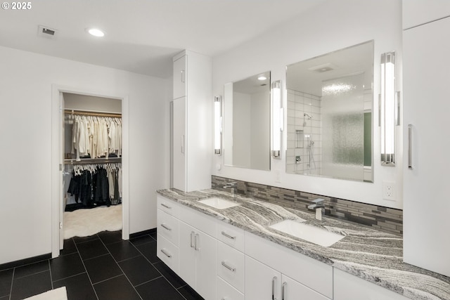 full bath with tasteful backsplash, double vanity, a walk in closet, and a sink