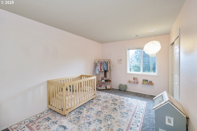 bedroom with visible vents, a nursery area, baseboards, and carpet floors