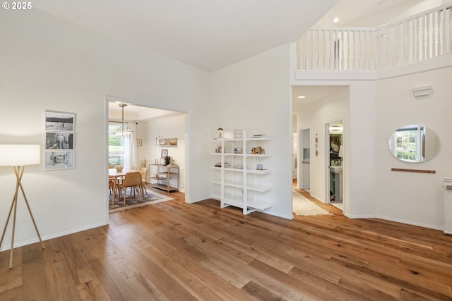 unfurnished living room with a chandelier, a high ceiling, baseboards, and hardwood / wood-style flooring