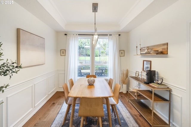 dining area with a decorative wall, a wainscoted wall, a tray ceiling, and wood finished floors