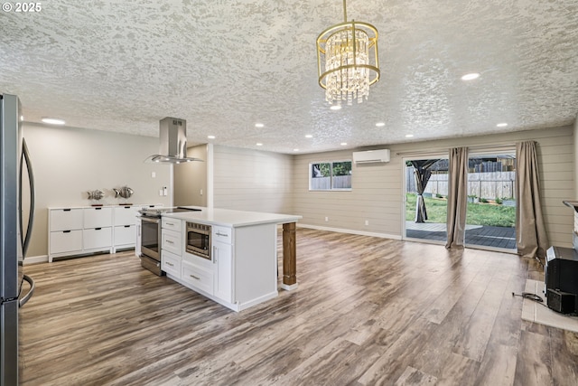 1213 NW Westridge St, Vancouver, WA 98665 - kitchen with island exhaust hood, a wall mounted AC, appliances with stainless steel finishes, wood finished floors, and white cabinets