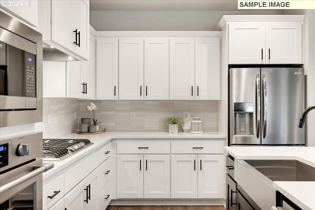 kitchen with sink, backsplash, white cabinets, and appliances with stainless steel finishes