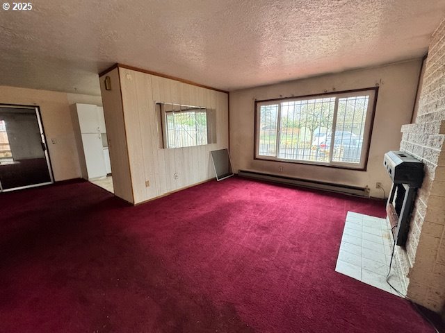 unfurnished living room with a baseboard heating unit, carpet flooring, a fireplace, and a textured ceiling