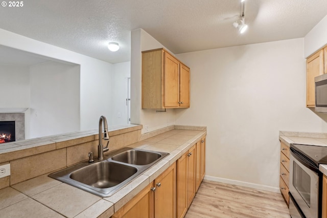 kitchen featuring sink, a textured ceiling, light hardwood / wood-style flooring, a tile fireplace, and stainless steel appliances